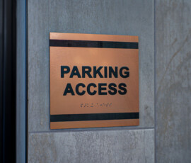 Copper parking access sign on a gray concrete wall with Braille beneath.