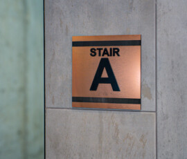 Copper stair sign reading 'STAIR A' mounted on a gray stone wall