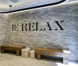Interior lounge with a gray brick accent wall and a large BERLEX sign, plus wooden benches and circular stools in front of it.