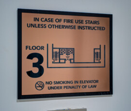 Orange safety sign with fire escape instructions and floor plan diagram mounted on a wall (partial view).