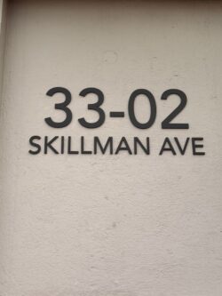 Address sign on a beige wall reading '33-02' above 'SKILLMAN AVE' (Skillman Ave address plate).
